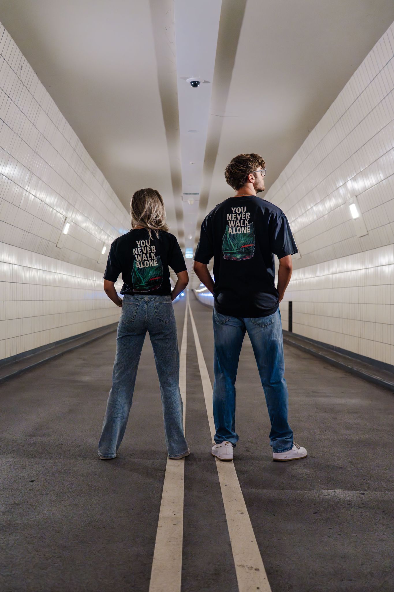 Oversized T-shirt met opdruk “YOU NEVER WALK ALONE” en illustratie van De Kuip, Erasmusbrug en skyline van Rotterdam in groen-rood kleurenpalet.
