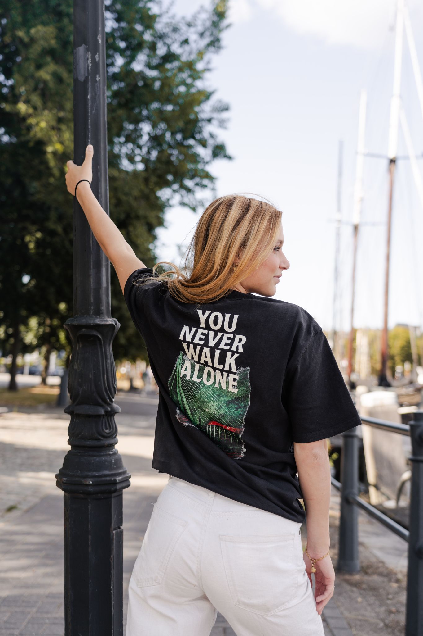 Oversized T-shirt met opdruk “YOU NEVER WALK ALONE” en illustratie van De Kuip, Erasmusbrug en skyline van Rotterdam in groen-rood kleurenpalet.
