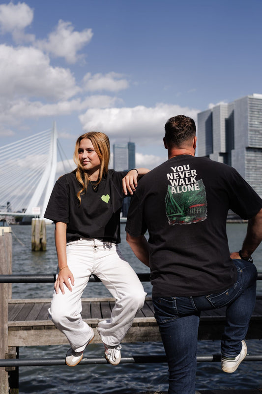 Oversized T-shirt met opdruk “YOU NEVER WALK ALONE” en illustratie van De Kuip, Erasmusbrug en skyline van Rotterdam in groen-rood kleurenpalet.